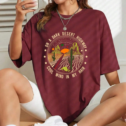 Woman wearing a maroon t-shirt with a graphic design, sitting on a wooden floor.