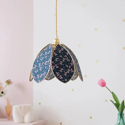 Decorative pendant light with floral patterns hanging in a room with a pink wall and a vase with a tulip.