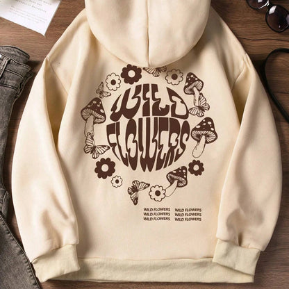 Beige hoodie with 'Wild Flowers' design on a wooden surface with shoes and sunglasses.