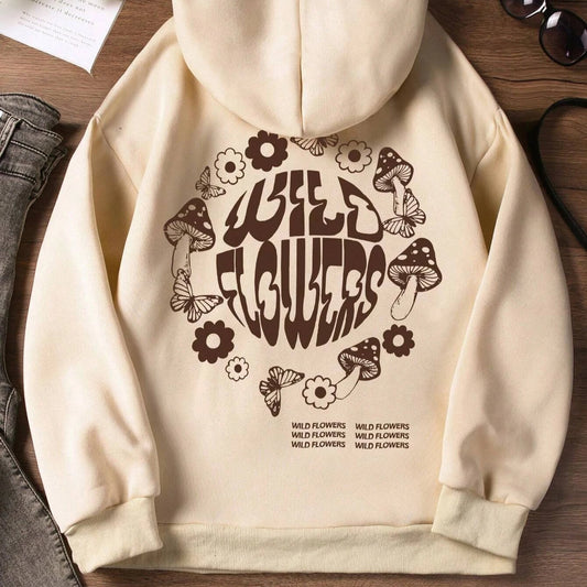 Beige hoodie with 'Wild Flowers' design on a wooden surface with shoes and sunglasses.